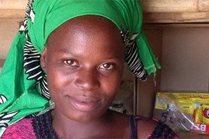 A smallholder farmer wearing a bright green head wrap stands in front of her insured seeds.