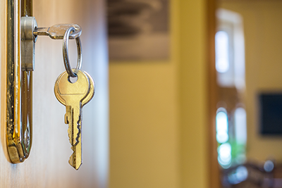 Closeup of a key in the door of a new home. Interior of home is seen in the background.